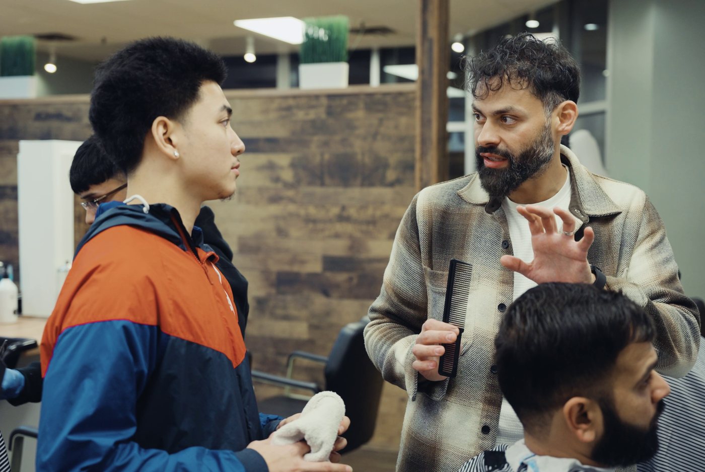 An instructor coaching a student beside a client in the chair